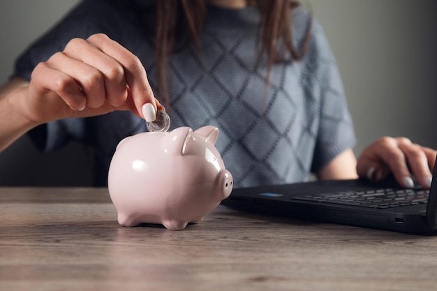 Woman hand putting money coin into piggy bank