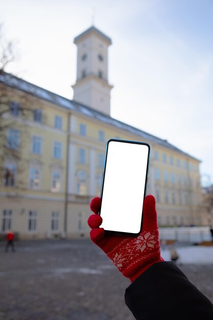 背景に白い画面のリヴィウ市庁舎と電話を保持している赤い手袋をはめた女性の手