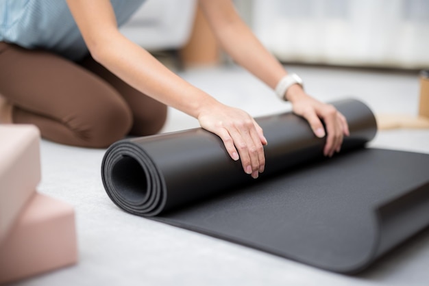 Женщина вручную скручивает коврик для йоги дома