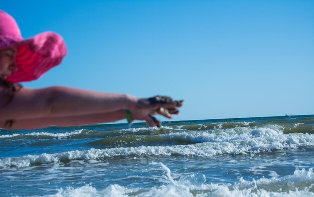 Woman hand in sea against clear blue sky