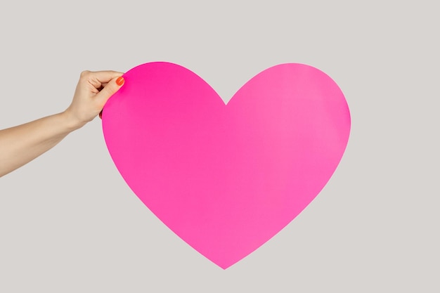 Woman hand showing big pink paper heart symbol of love and devotion