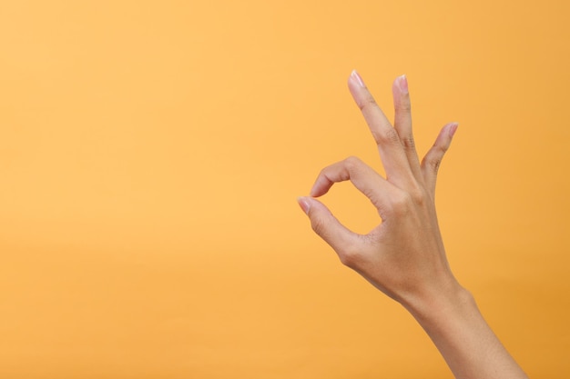 Woman hand showing ok gesture isolated on a yellow background