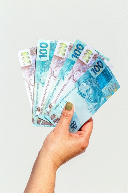 Photo woman hand showing one hundred and two hundred reais bills on isolated surface