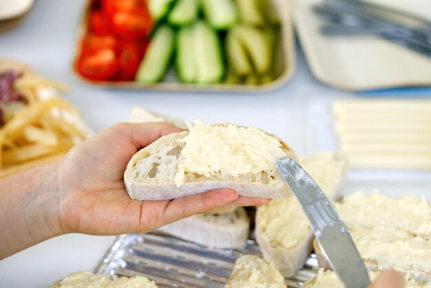 女性の手は、グリルパーティーのために軽食を準備するプロセスにんにくとチーズサラダでパンを広げます