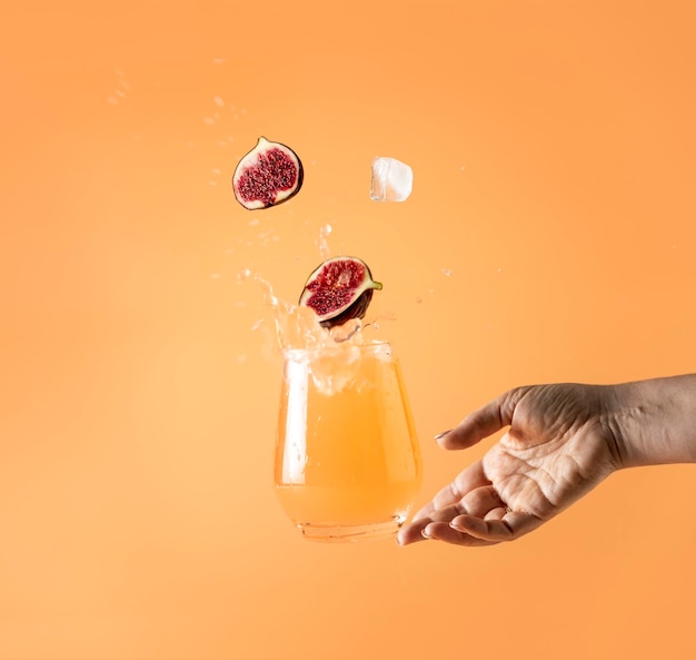 Woman hand support fly glass of pink cocktail drink with splash juice slice fig falling in glass Summer art food concept on peach color background