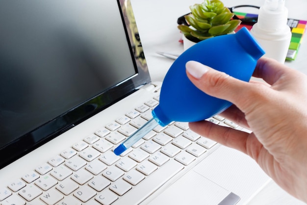 Mano della donna che spazza la polvere dalla tastiera del computer portatile usando la lampadina dell'aria