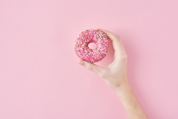 woman hand take color donut on pink. creativity minimalism style food concept, top view