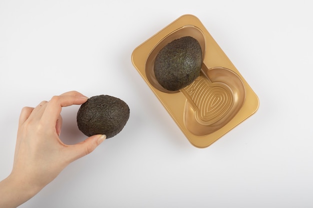 Woman hand taking a brown avocado isolated on white-gray table. 