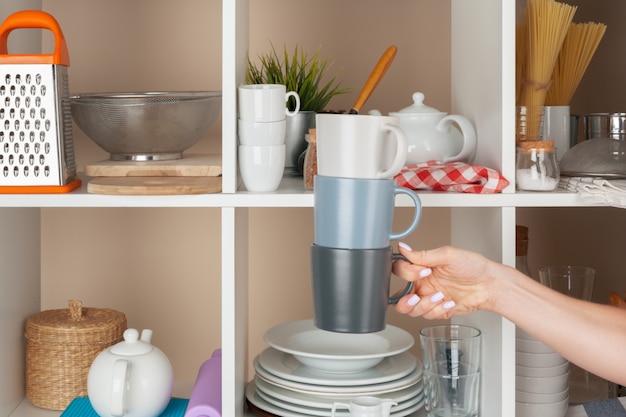 Woman hand taking dishware pieces from shelf in kitchen