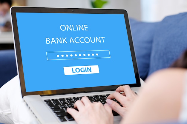 Рука женщины связывая портативный компьютер с логином пароля банковского счета онлайн на экране дома