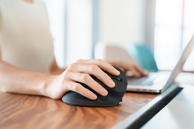 写真 コンピューターの人間工学に基づいたマウスを使用する女性の手は、長い時間働くため手首の痛みを防ぎます。ド・ケルバンの腱滑膜炎の交差点症状手根管症候群またはオフィス症候群の概念