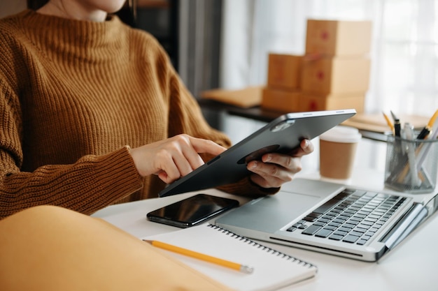 Woman hand using a laptop smartphone and tablet and writing notebook at the office of her business online shopping