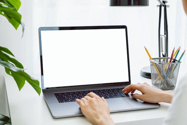 La mano della donna che per mezzo del computer portatile sulla tavola in casa, deride su dello schermo in bianco.