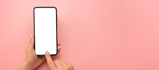 Woman hand using smartphone isolated on pink background Hand holding smartphone device and touching screen Close up view of woman using blank screen smartphone copy space wide image