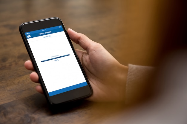 インターネットバンキングアプリケーションを介してオンラインでお金を転送するスマートフォンを使用して女性の手