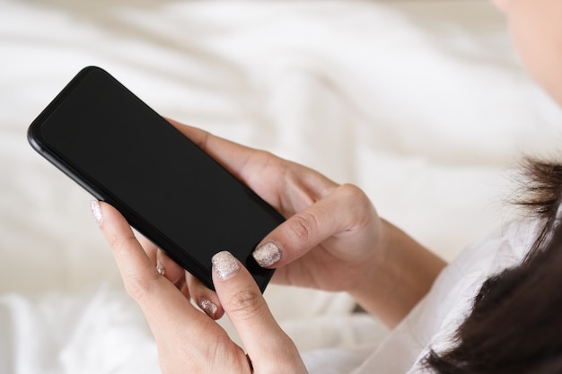 Foto mano della donna che utilizza smartphone con lo schermo in bianco mentre si trovava a letto al mattino.