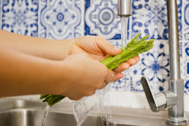 台所の流しでグリーンアスパラガスを手洗いする女性