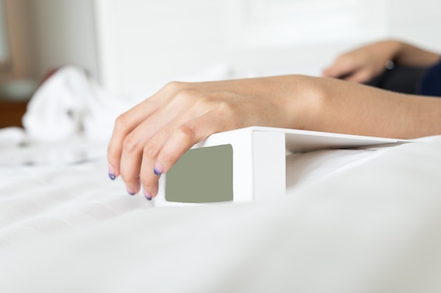 Woman hand on white digital alarm clock in bedroom