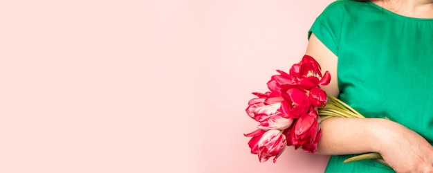 Woman hand with manicure holding tulips flowers on pink background