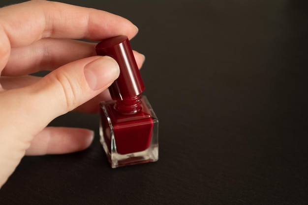 Woman hand with manicured nails opening small bottle with red nail polish