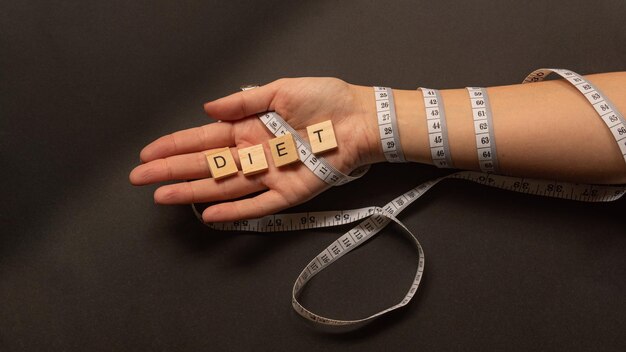 Foto mano della donna con un metro intorno che tiene una lettera di concetto di dieta blocca su uno sfondo nero