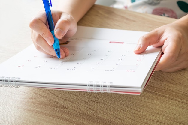 Mano della donna con la scrittura della penna sul concetto di riunione dell'appuntamento di pianificazione aziendale della data del calendario