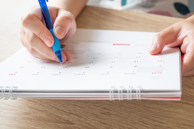 Foto mano della donna con la scrittura della penna sul concetto di riunione dell'appuntamento di pianificazione aziendale della data del calendario