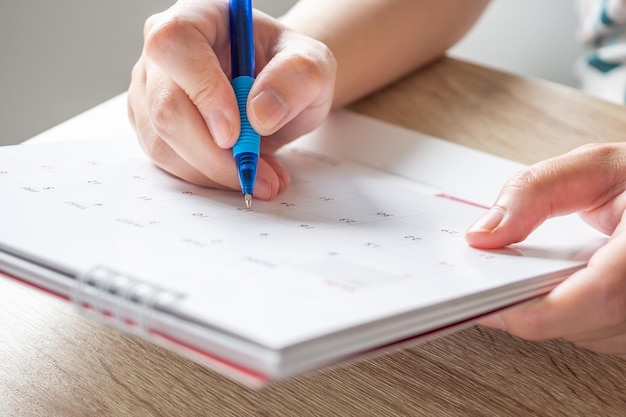 Foto mano della donna con la scrittura della penna sul concetto di riunione dell'appuntamento di pianificazione aziendale della data del calendario