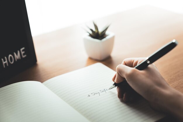 Foto mano di donna con matita che scrive stare al sicuro sul quaderno a casa scrivania lavoro da casa concetto di epidemia