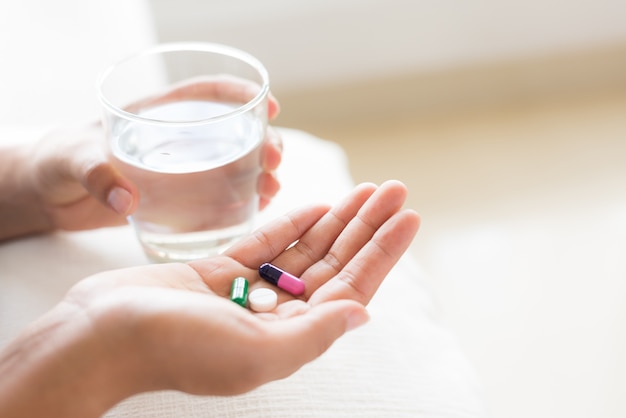 Woman hand with pills and glass of water for headache treatment. Healthcare concept.