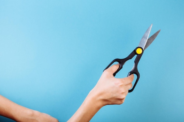 Mano della donna con le forbici isolate sul blu