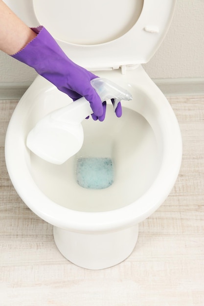 Woman hand with spray bottle cleaning a toilet bowl in a bathroom