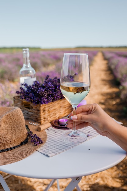 Woman hand with white wine glass on a lavander fields\
background in provence france lines of purple flowers bushes