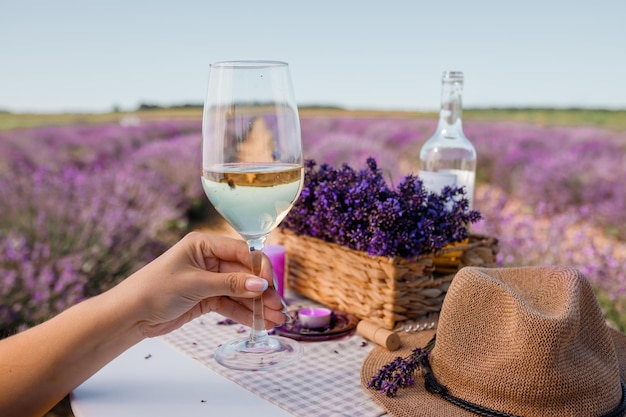 Woman hand with white wine glass on a lavander fields\
background in provence france lines of purple flowers bushes