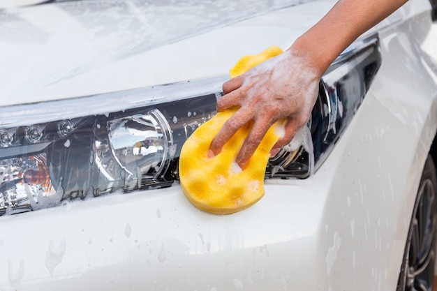 Woman hand with yellow sponge washing headlight modern car or cleaning automobile. 