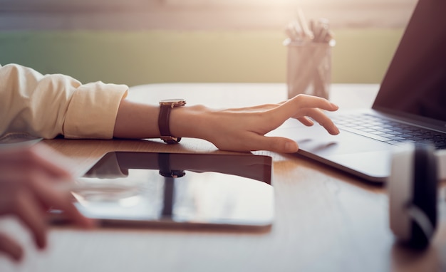 Woman hand working on tablet and press laptop on the table in office.