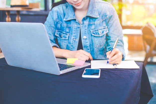 Woman hand works in a laptop computer and is writing on notepad 