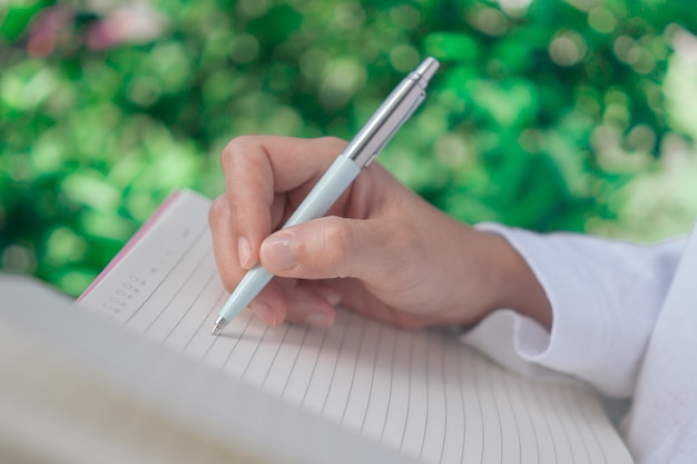 Woman hand writing down in small white memo notebook