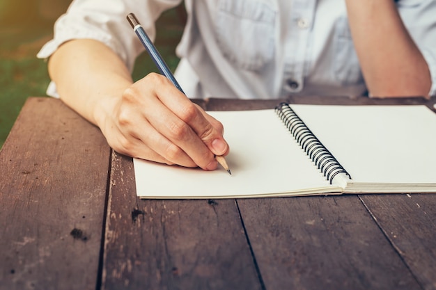 Photo woman hand writing note pad on wood table in coffee shop.