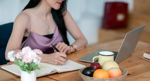 Woman hand writing on a notebook while sitting at the table.