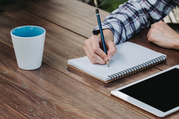 Woman hand writing notepad and holding phone on wooden table at coffee shop