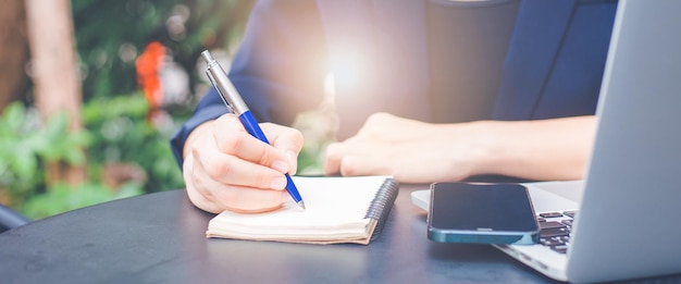 Foto mano della donna che scrive su un blocco note con una penna nell'ufficio. banner web.