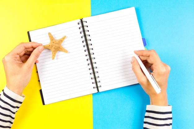 Woman hand writing in open travel notebook over blue and yellow background