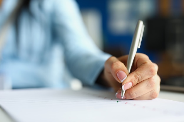 Женщина почерков с серебряной шариковой ручкой в блокноте крупным планом