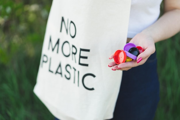 写真 女性の手は、環境汚染の概念を色とりどりのプラスチック製のふたの一握りを保持しています