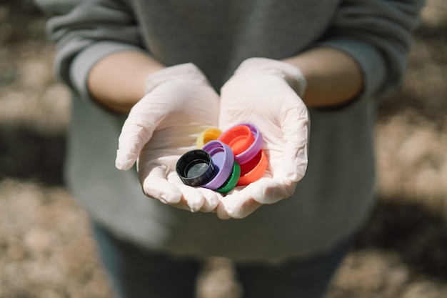 女性の手は、環境汚染のエコフレンドリーな行動のコンセプトに、カラフルなプラスチックのふたをいくつか持っている