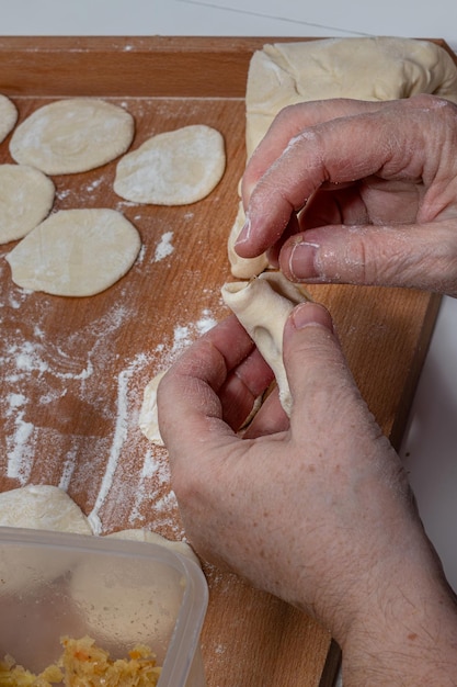 woman hands are making a damp dumpling On the wooden counter top are some raw dumplings in flour