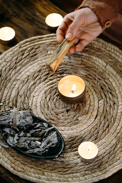 Woman hands burning palo santo before ritual on the table with candles and green plants smoke of