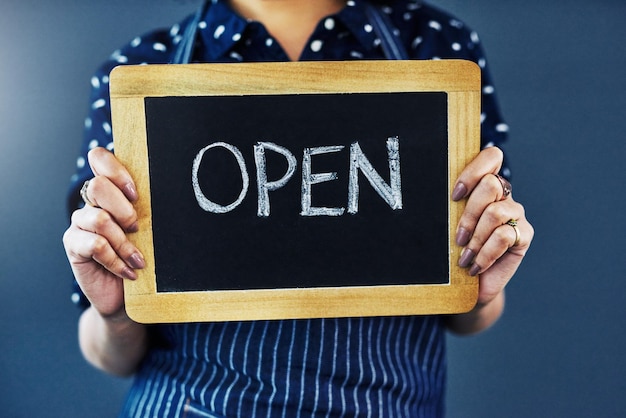 Woman hands and chalkboard with open sign for welcome or introduction on a studio background Closeup of female person or waitress with billboard or poster ready for service at cafe or restaurant