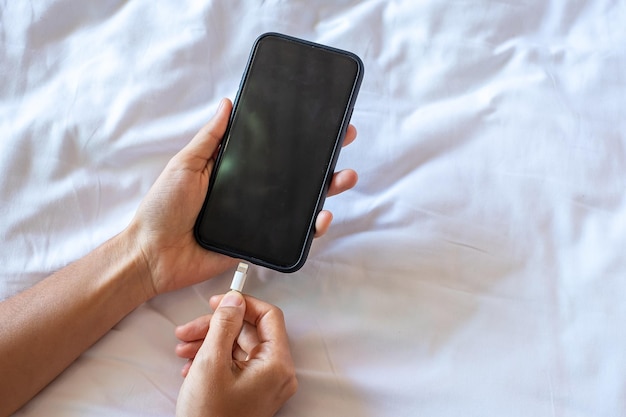 Woman hands charging battery in mobile smart phone in the\
bedroom at home technology multiple sharing and lifestyle\
concepts